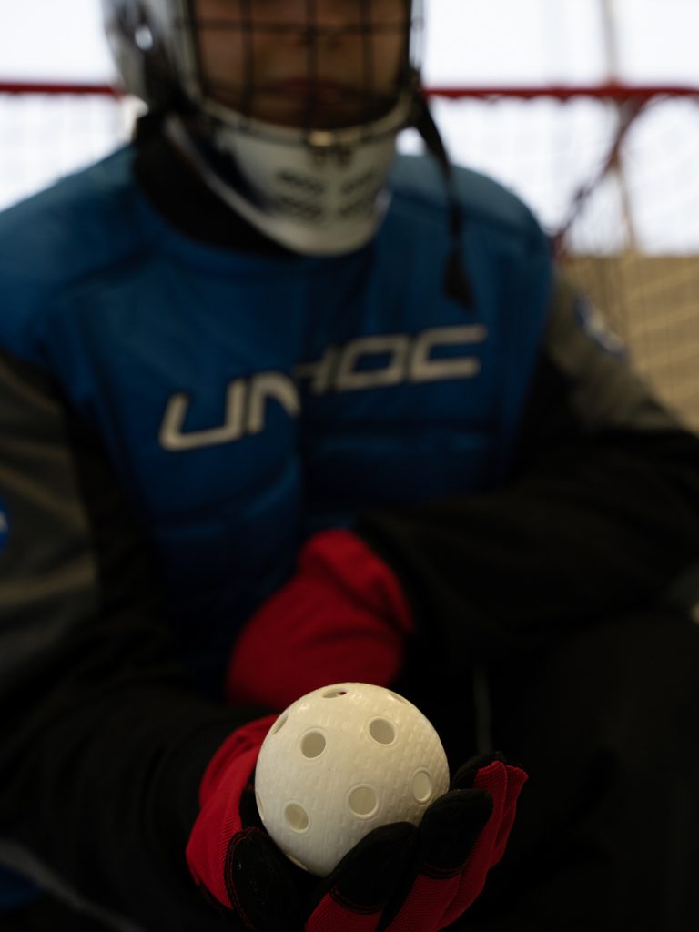 Der Torhüter zeigt einen Floorball. Er ist aus Kunststoff, hat ca.8cm Durchmesser und viele Löcher.