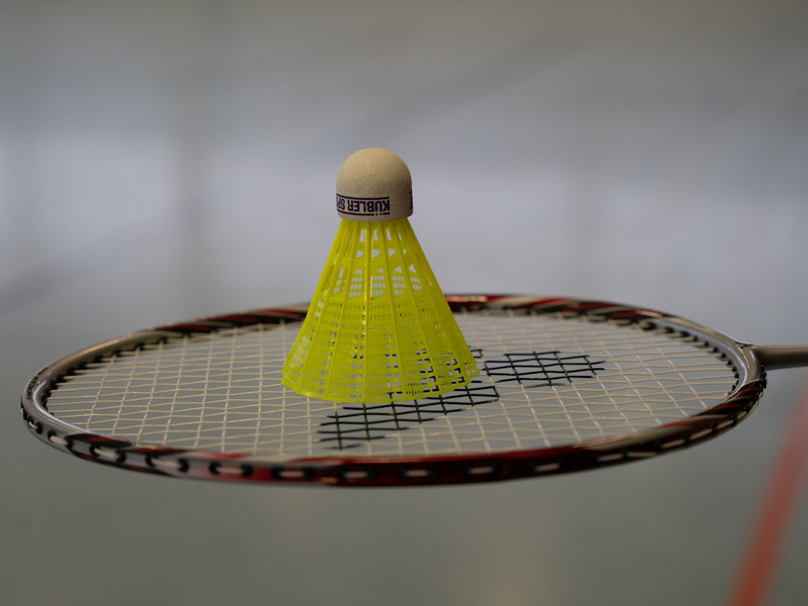 Symbolbild Badminton: Ein gelber Federball befindet sich auf einem Badmintonschläger.