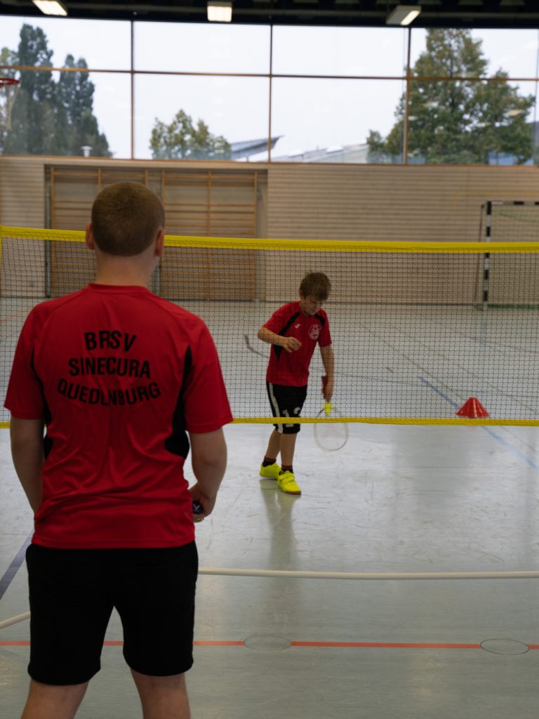 Ein Teilnehmer wartet konzentriert am Netz. Der andere Teilnehmer wird gleich mit dem Aufschlag (Serve) den Federball in das Spiel bringen.