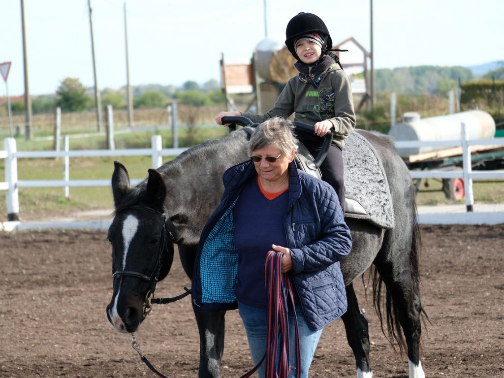 Die Trainerin führt das Pferd und gibt dem Kind Hinweise zur Körperhaltung und den einzelnen Aufgaben.